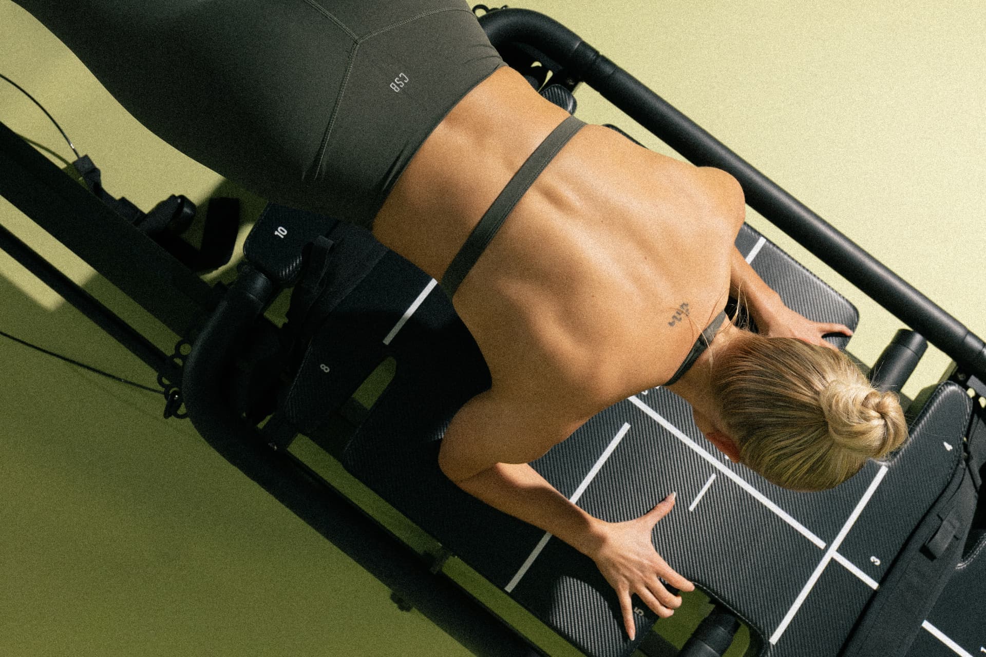 Overhead view of a woman training on a reformer against an olive-green wall